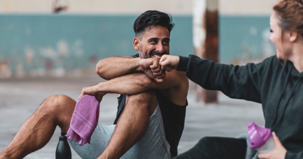 男人和女人锻炼后坐在健身房的地板上碰拳头。