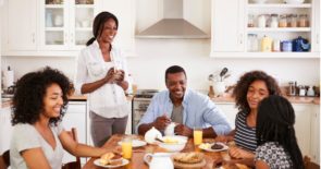 母亲，父亲和三个十几岁的女儿在厨房的餐桌上一起吃早餐。