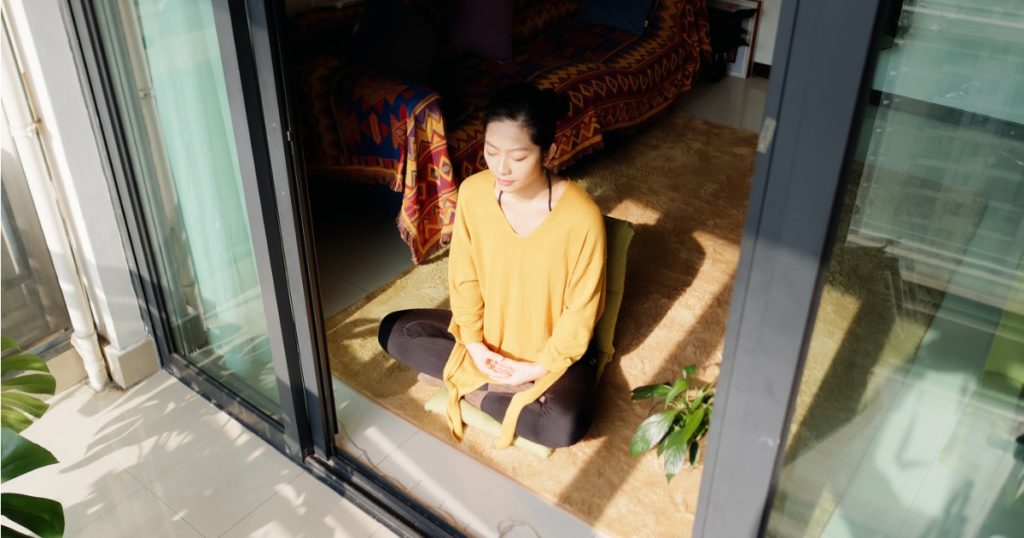 年轻的亚洲女性盘腿坐在打开的滑动玻璃门前的地板上。